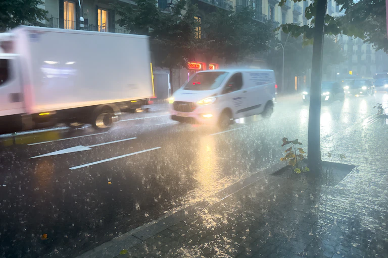 Vehicles circulen pel carrer sota una pluja intensa.