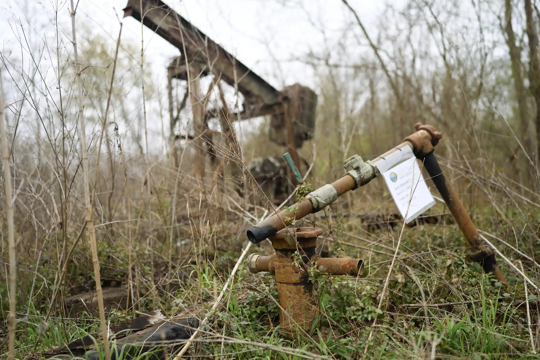 A rusting old piece of equipment sits in an area with low brush and a pipe sticking up out of the ground.