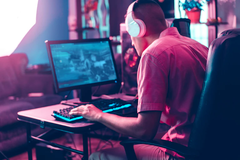 A man sits with headphones on playing a game on a laptop.