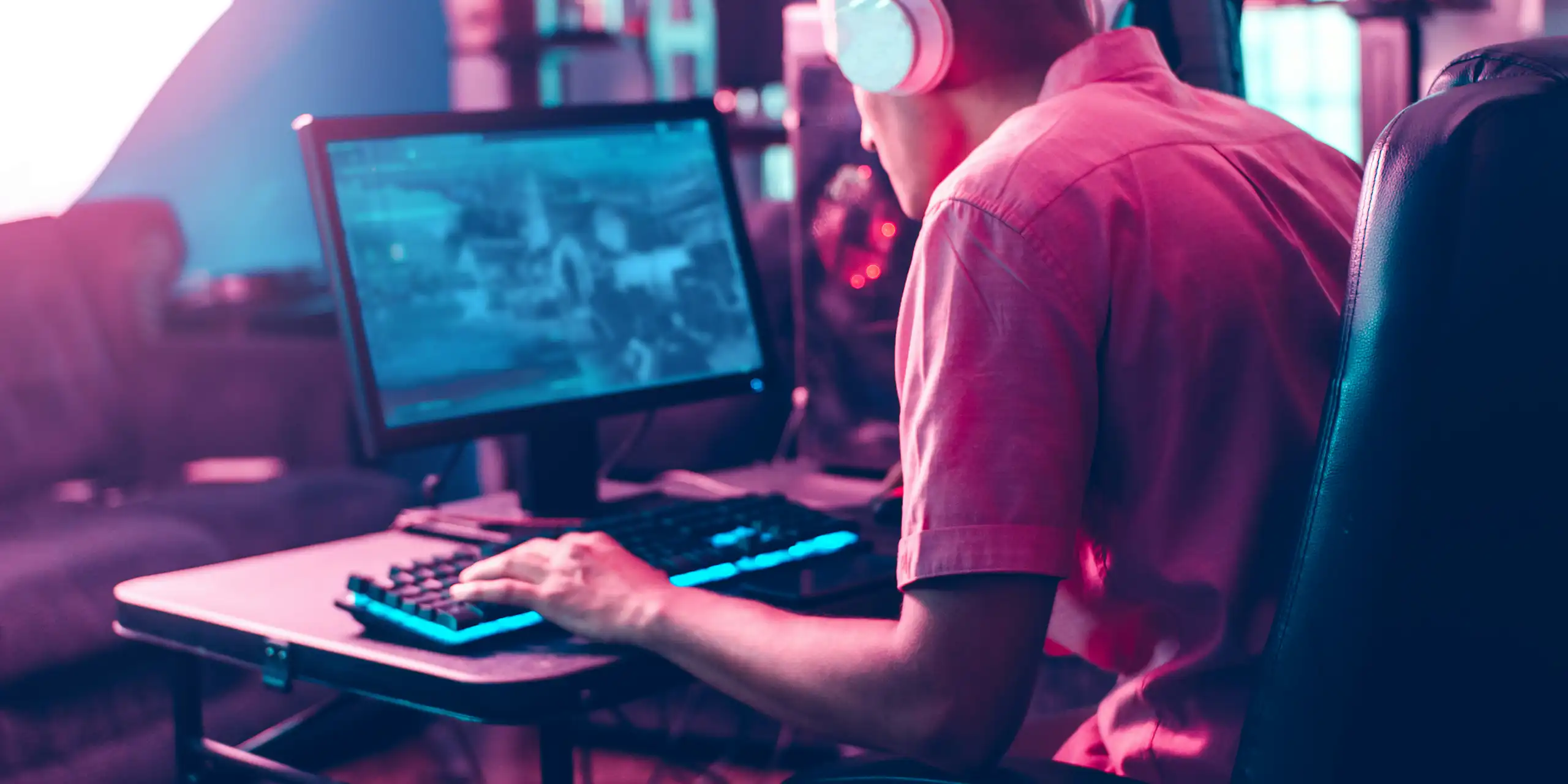 A man sits with headphones on playing a game on a laptop.