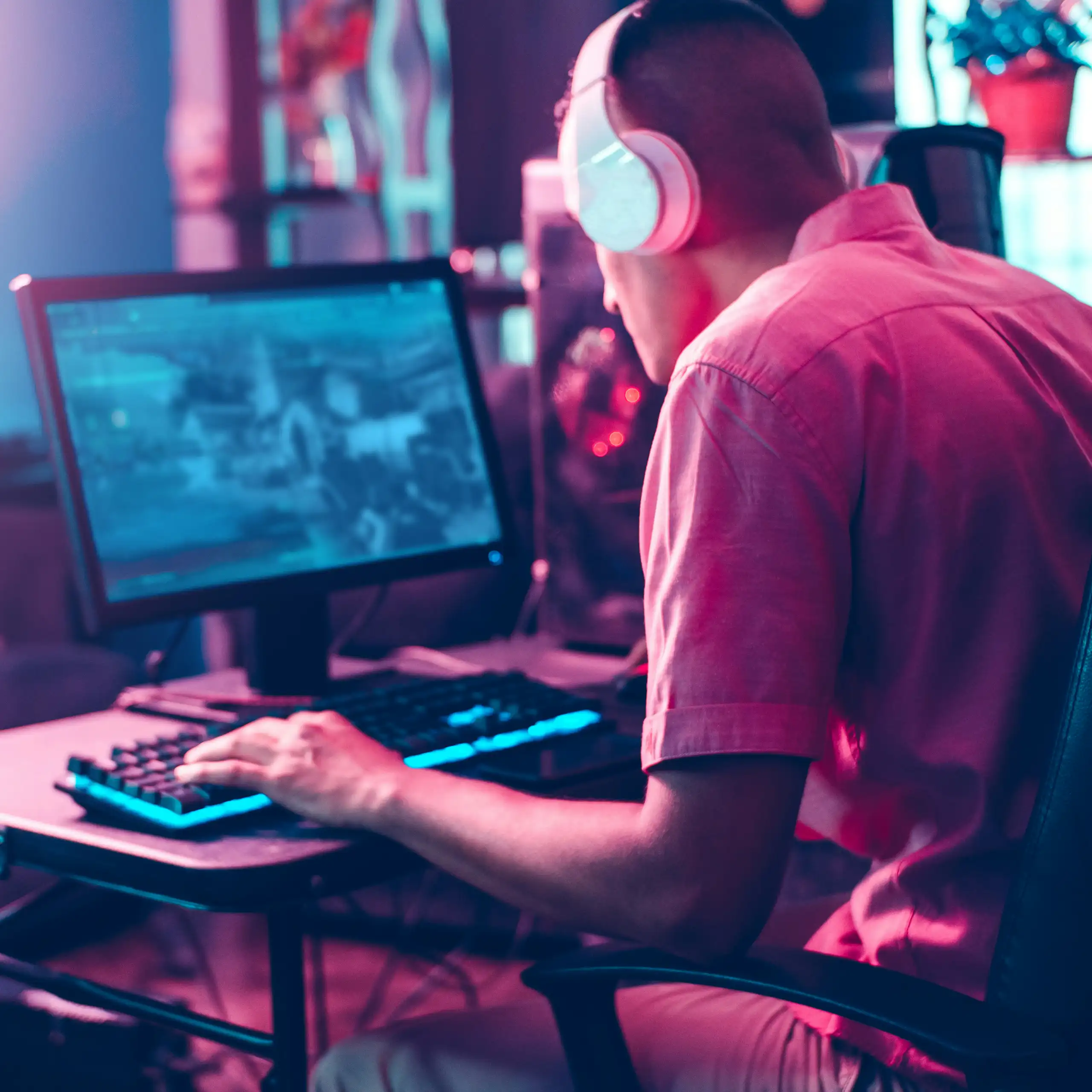 A man sits with headphones on playing a game on a laptop.
