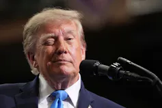 A man with fluffy orange-ish hair winks.