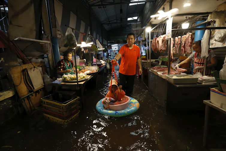 A man and his daughter wade through floodwater at a local market in Bangkok, Thailand.