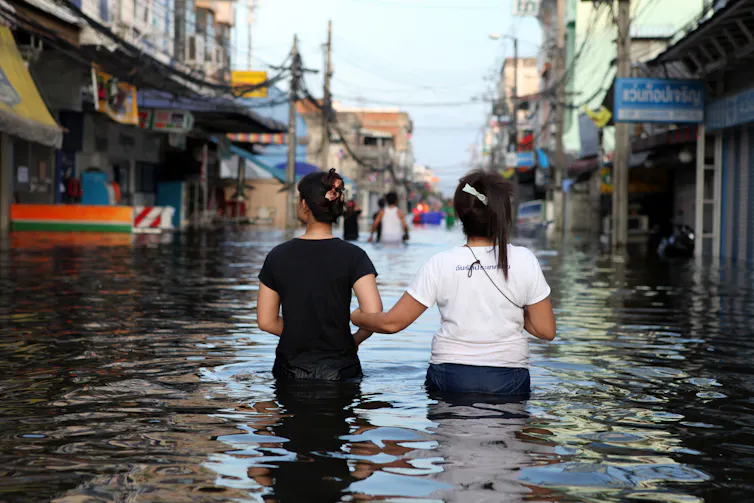 Two friends lock arms as they wade through a flooded street in Bangkok, Thailand.