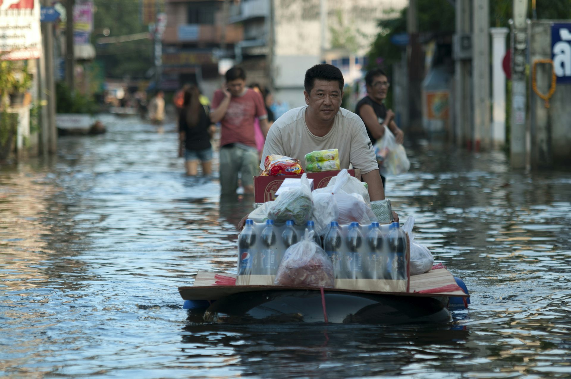 A man pushes a makeshift raft full of food supplies through a heavily flooded street in Bangkok, Thailand.