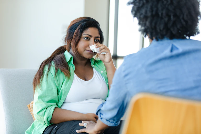 Pregnant woman wiping her nose while speaking with a therapist