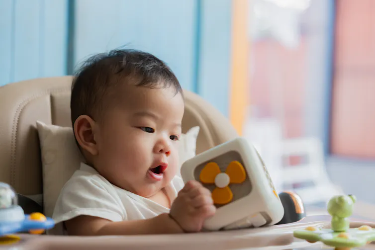 A baby in a high chair playing with an educational block toy