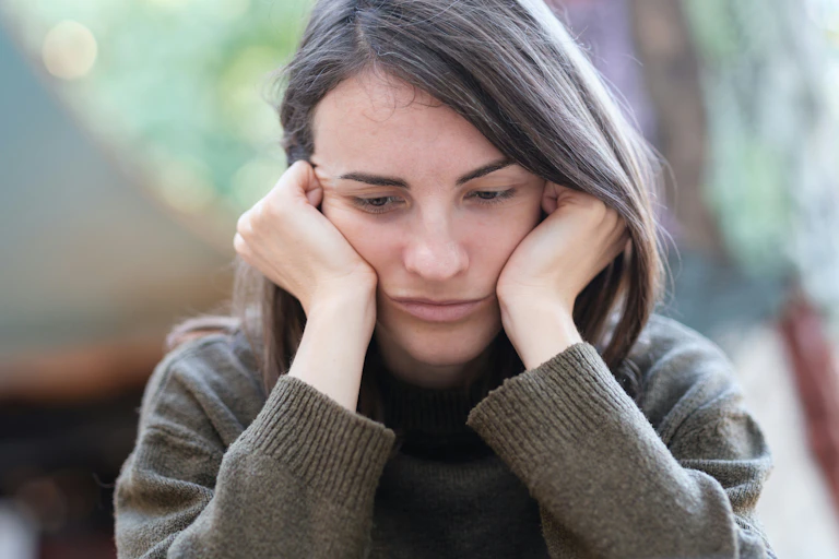 A woman in a grey jumper holding her face in her hands looking tired.