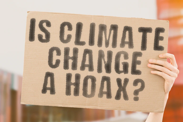cardboard sign with black pen, is climate change a hoax, hand holds sign up