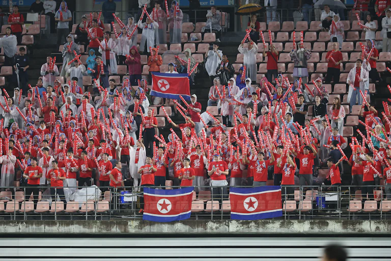 A large group of North Korean supporters cheer on their side from the stands during a football match.