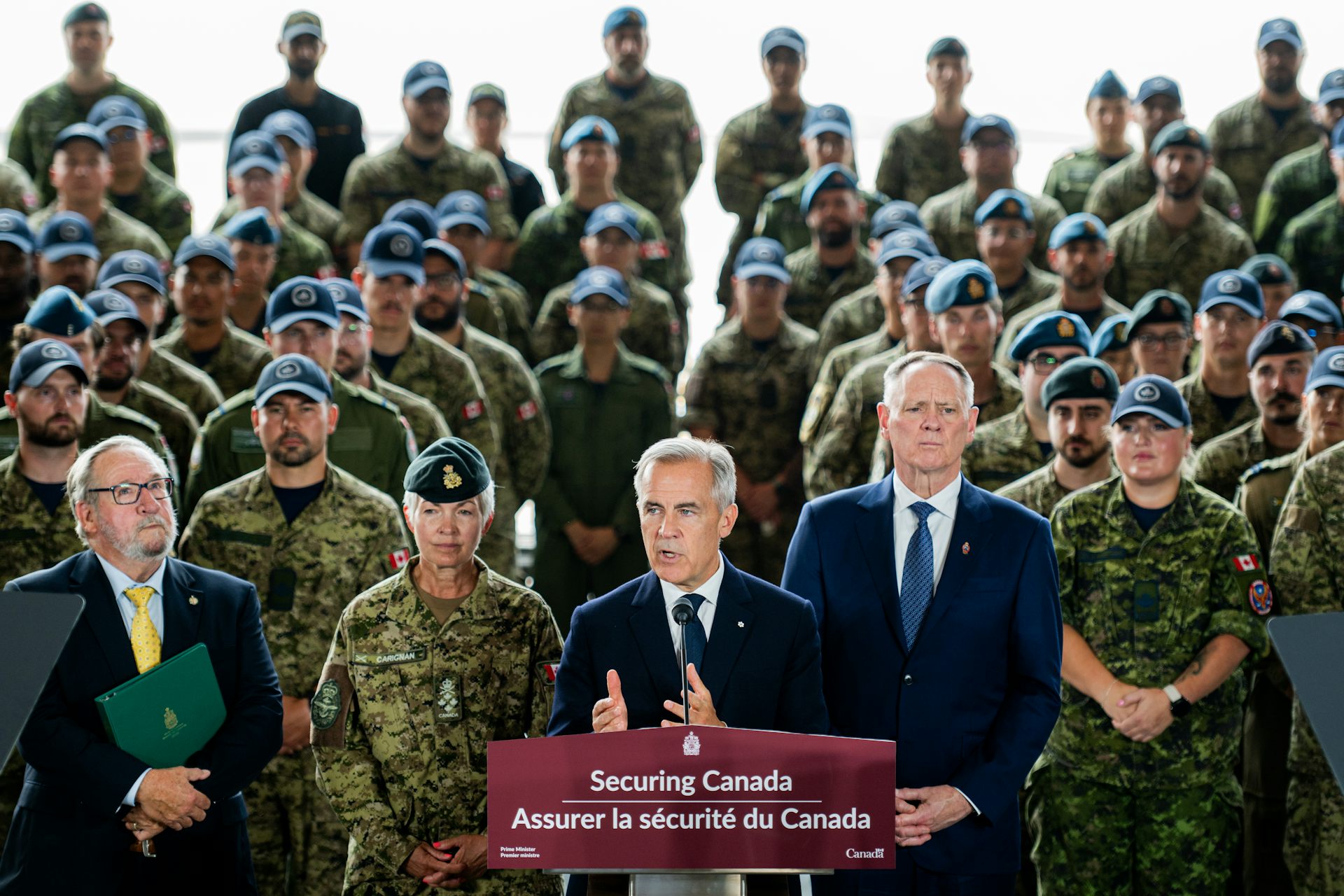 A slender man with short grey hair in front of a crowd of uniformed soldiers.