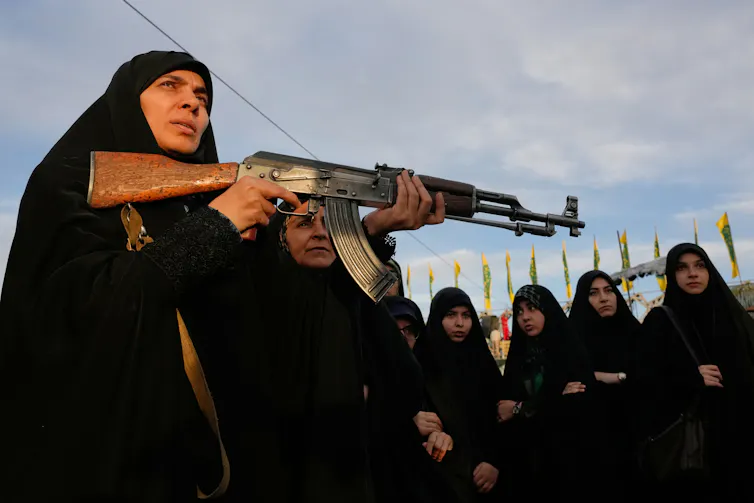 A woman in a niqab holds an assault rifle.
