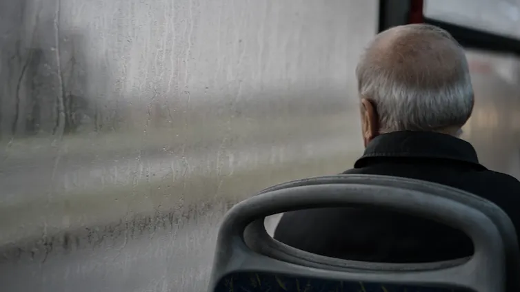 Back view of older man sitting on bus watching rain through the window