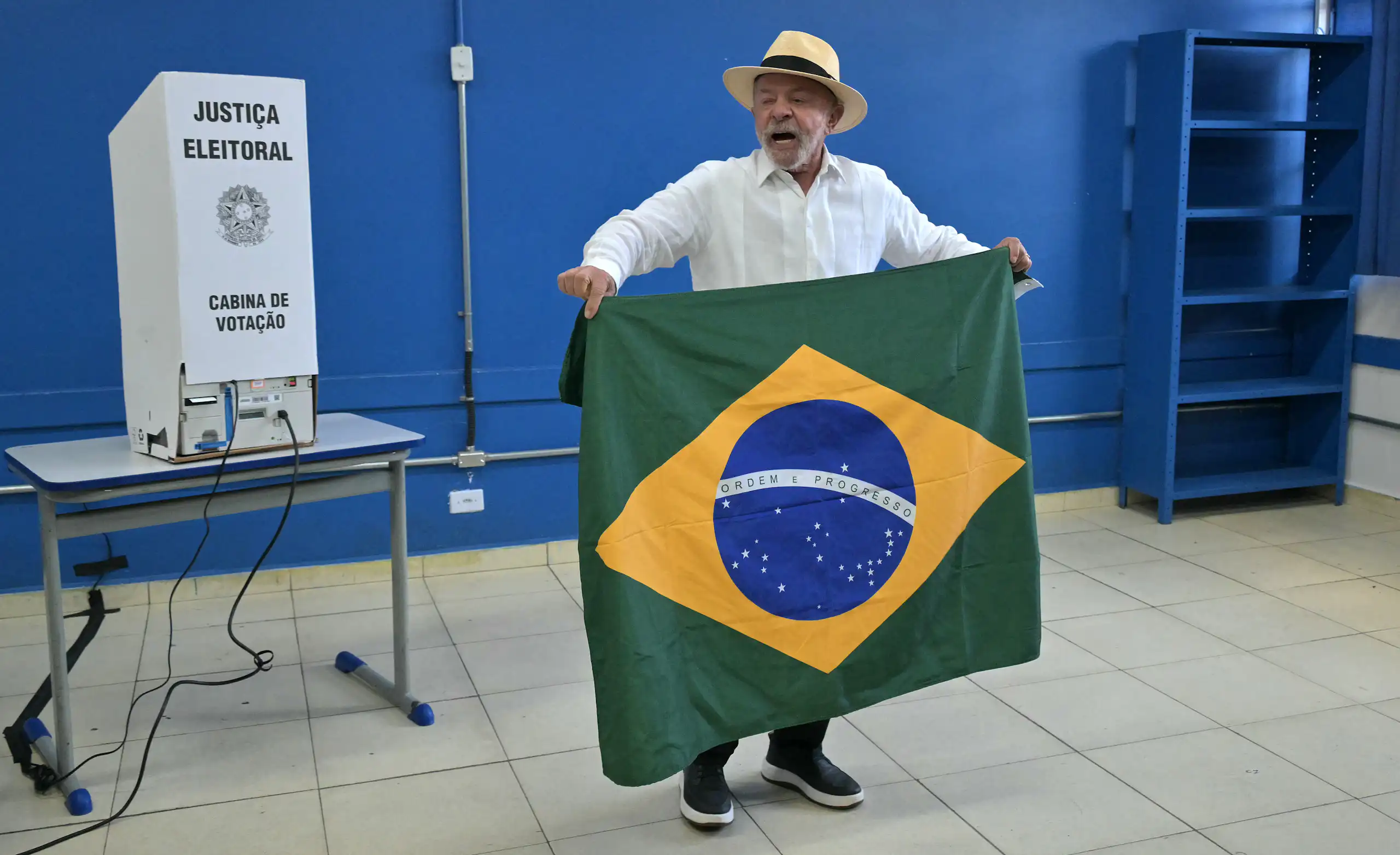 Lula devant une urne tient le drapeau brésilien en prenant la parole.