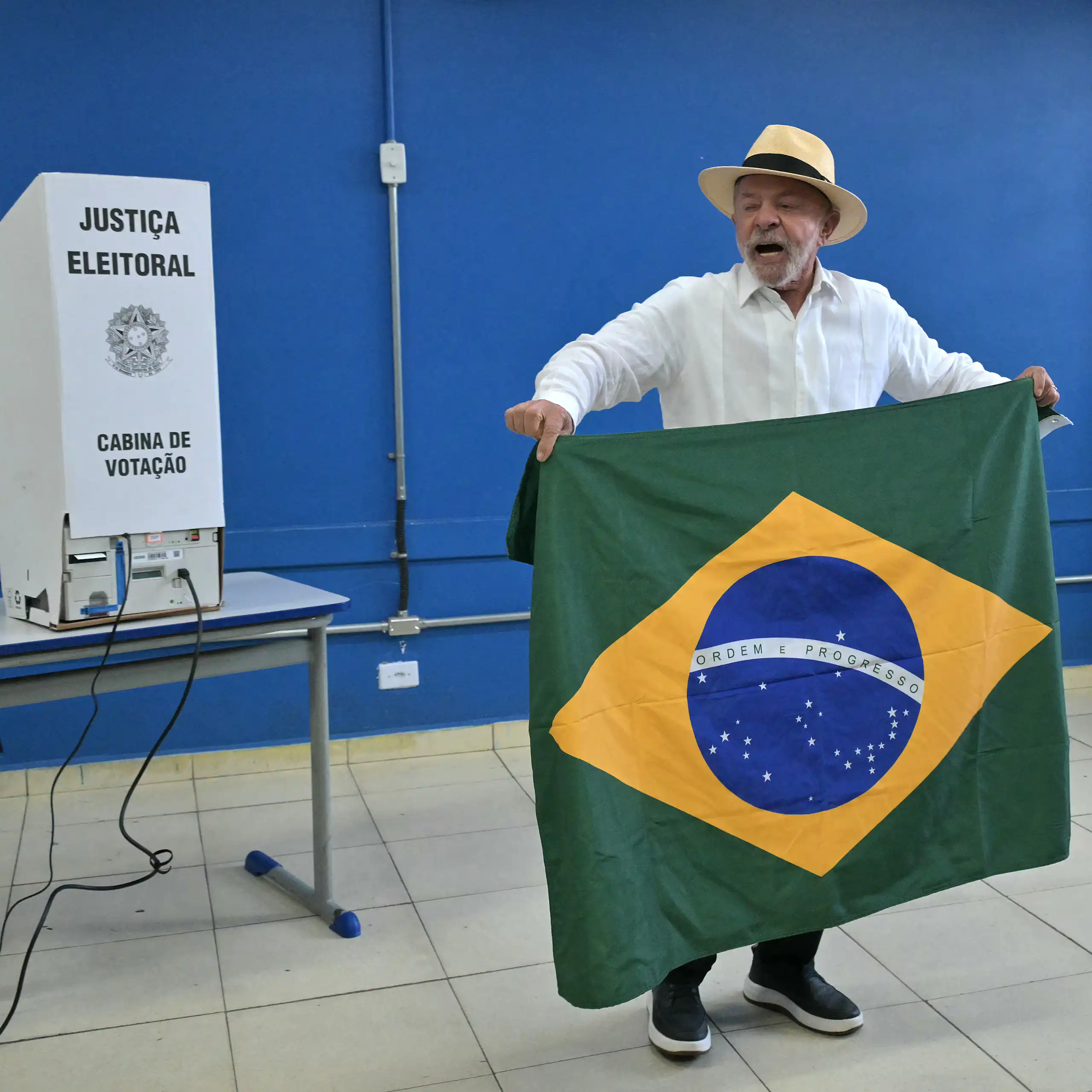 Lula devant une urne tient le drapeau brésilien en prenant la parole.