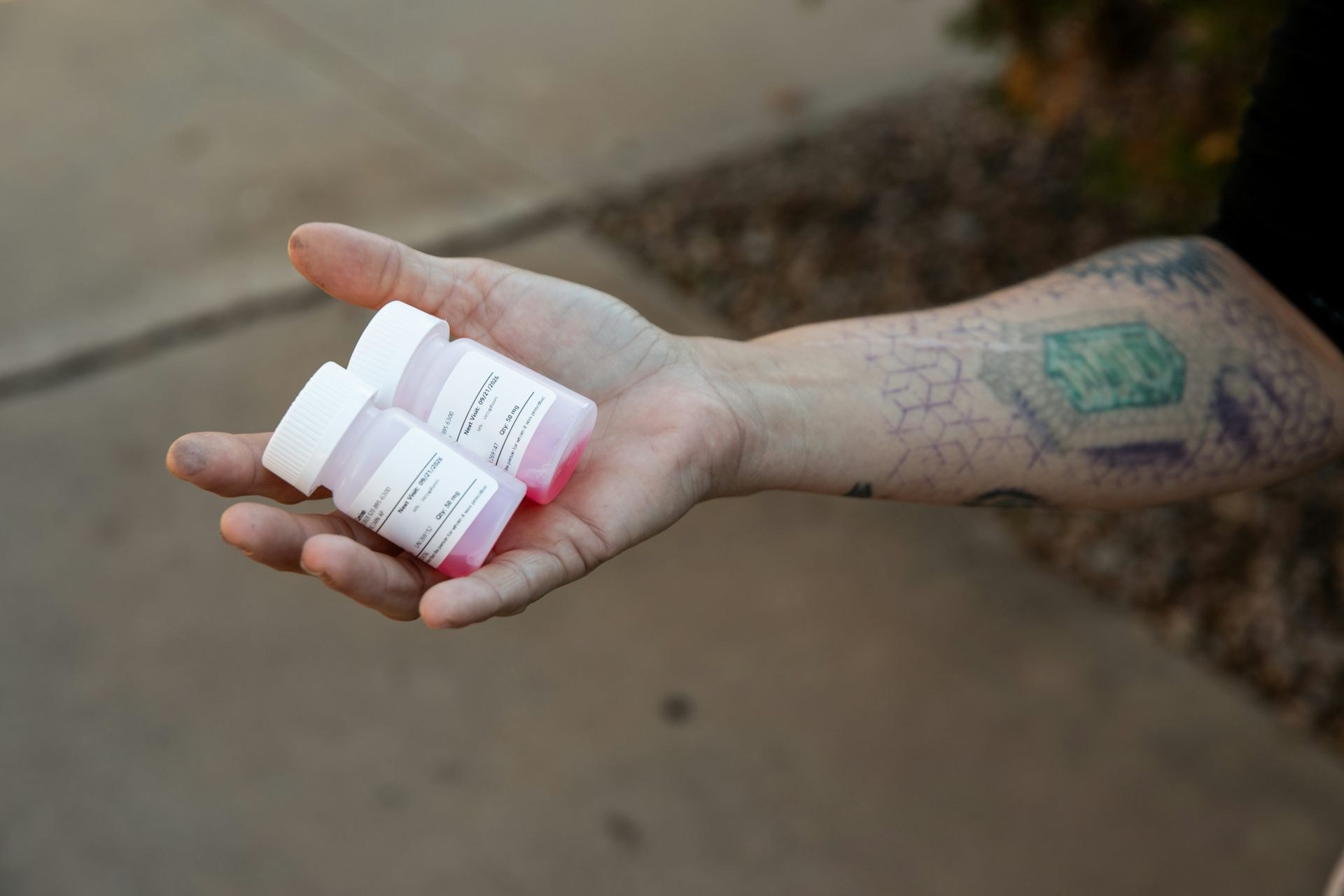 Two methadone bottles filled with red liquid in the palm of an outstretched hand.