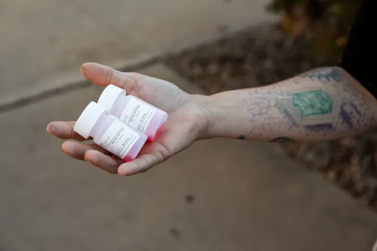 Two methadone bottles filled with red liquid in the palm of an outstretched hand.