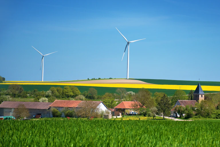 Vue panoramique : les champs de colza, le village et trois éoliennes.