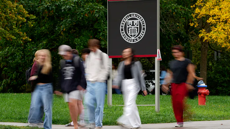 Des piétons passent devant un panneau de l’Université Cornell