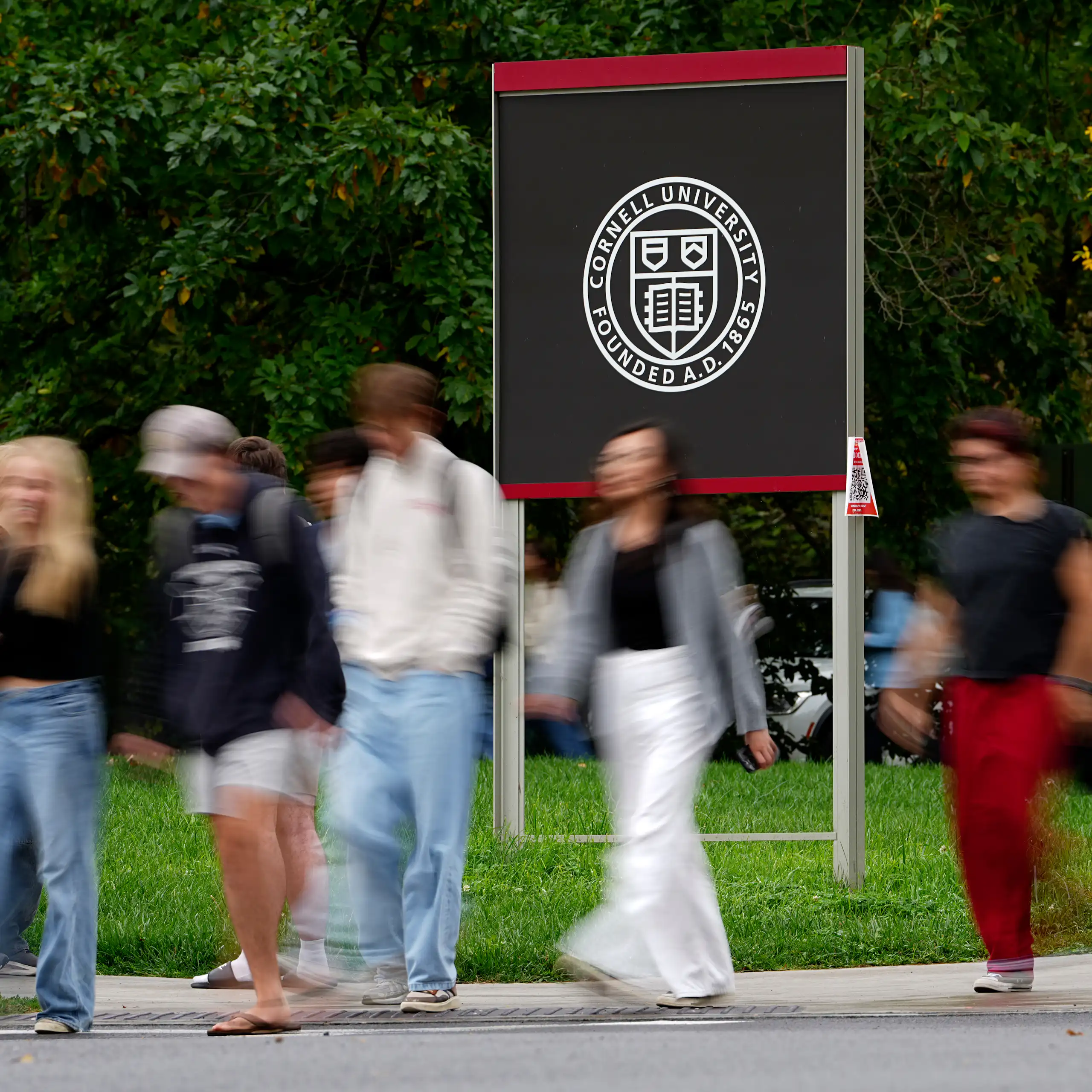 Pedestrians walk past a Cornell University sign