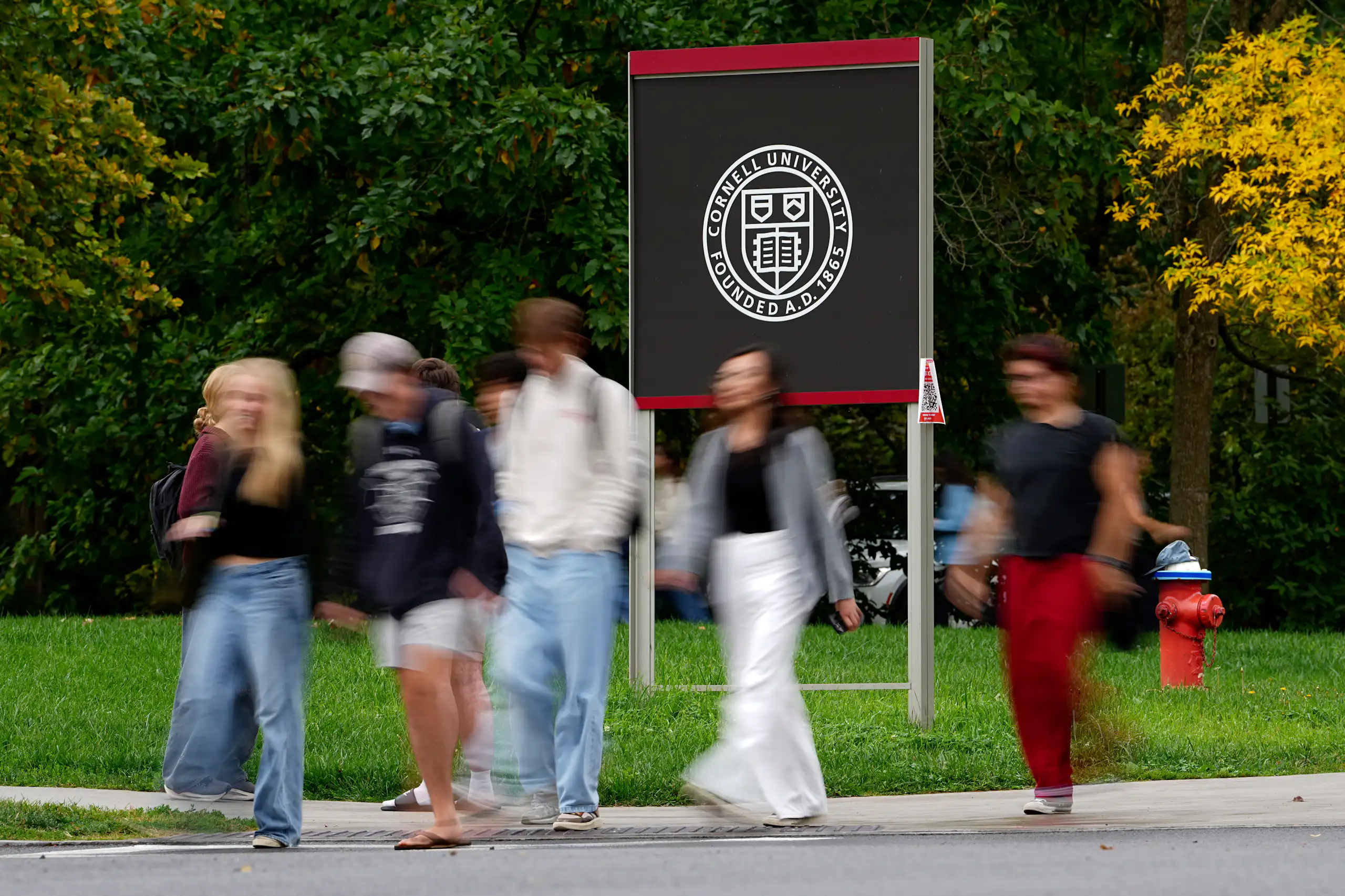 Pedestrians walk past a Cornell University sign
