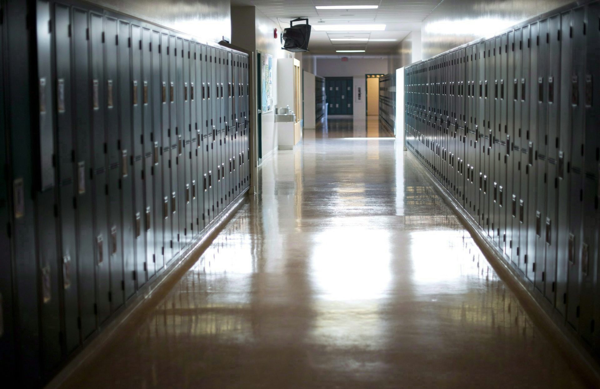 Lorong sekolah yang sepi dengan deretan loker di sepanjang dinding.