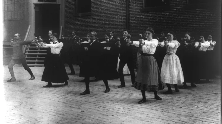 A group of Victorian people performing dumbbell exercises in an outdoor Washington gymnasium in 1899.