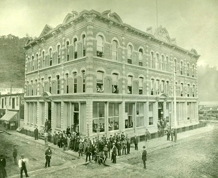 Businessmen are seen outside an ornate building in a black-and-white photo.