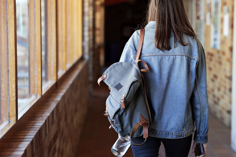 Back view of a young woman with backpack walking down a corridor at university.