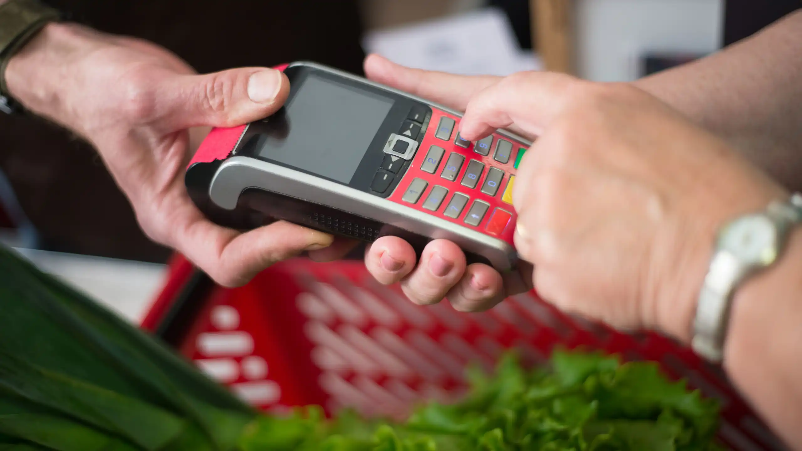 A grocer holding an EFTPOS machine up for a woman to pay for a basket of groceries