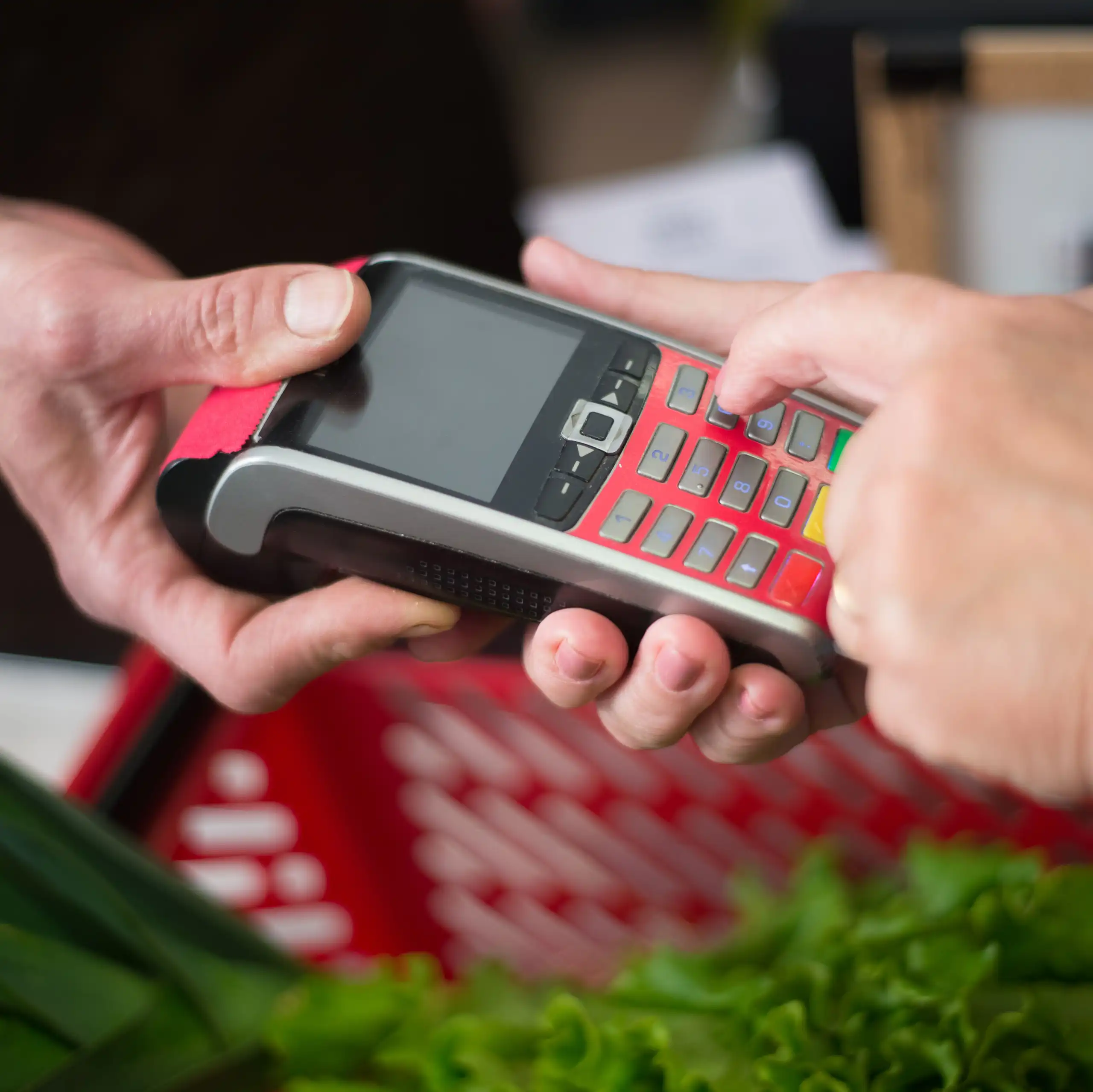 A grocer holding an EFTPOS machine up for a woman to pay for a basket of groceries