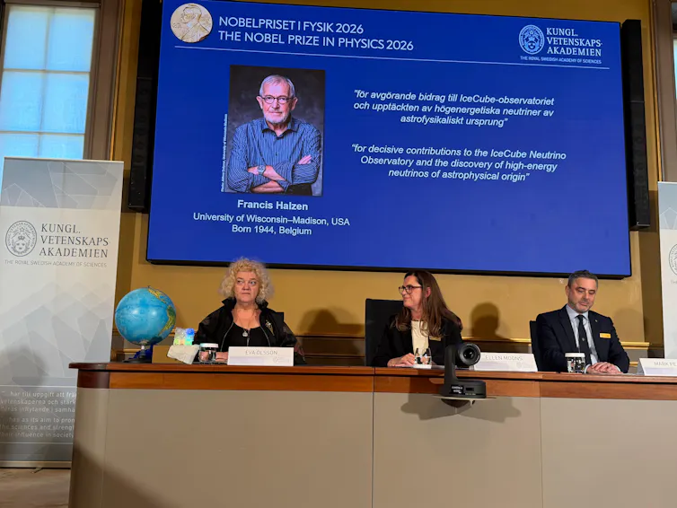 A panel of three people sitting at a table, with a screen behind them showing a photo of Francis Halzen and a description of his research.