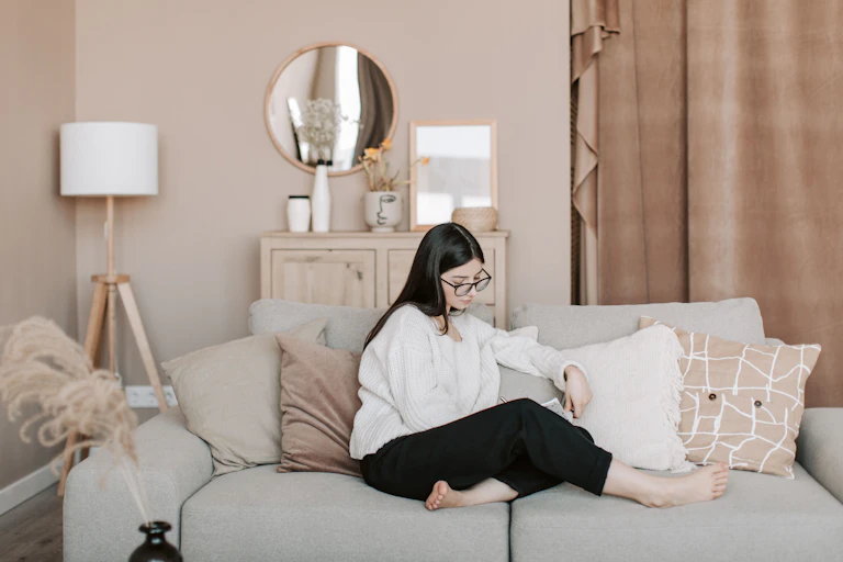 A young woman sits casually on a couch in a very blandly-coloured lounge.