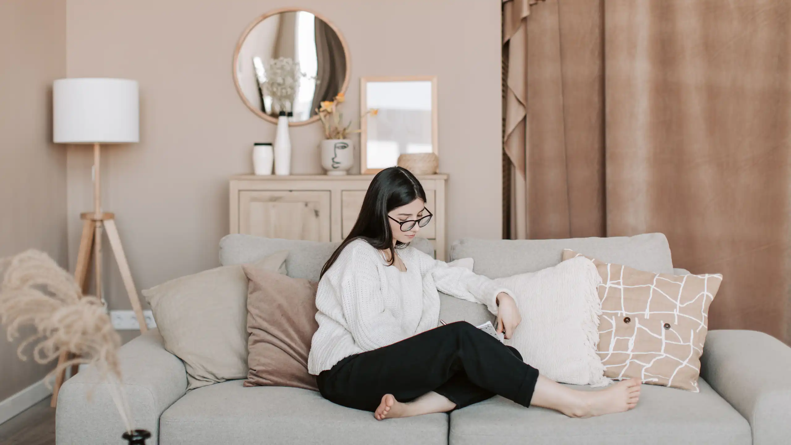 A young woman sits casually on a couch in a very blandly-coloured lounge.
