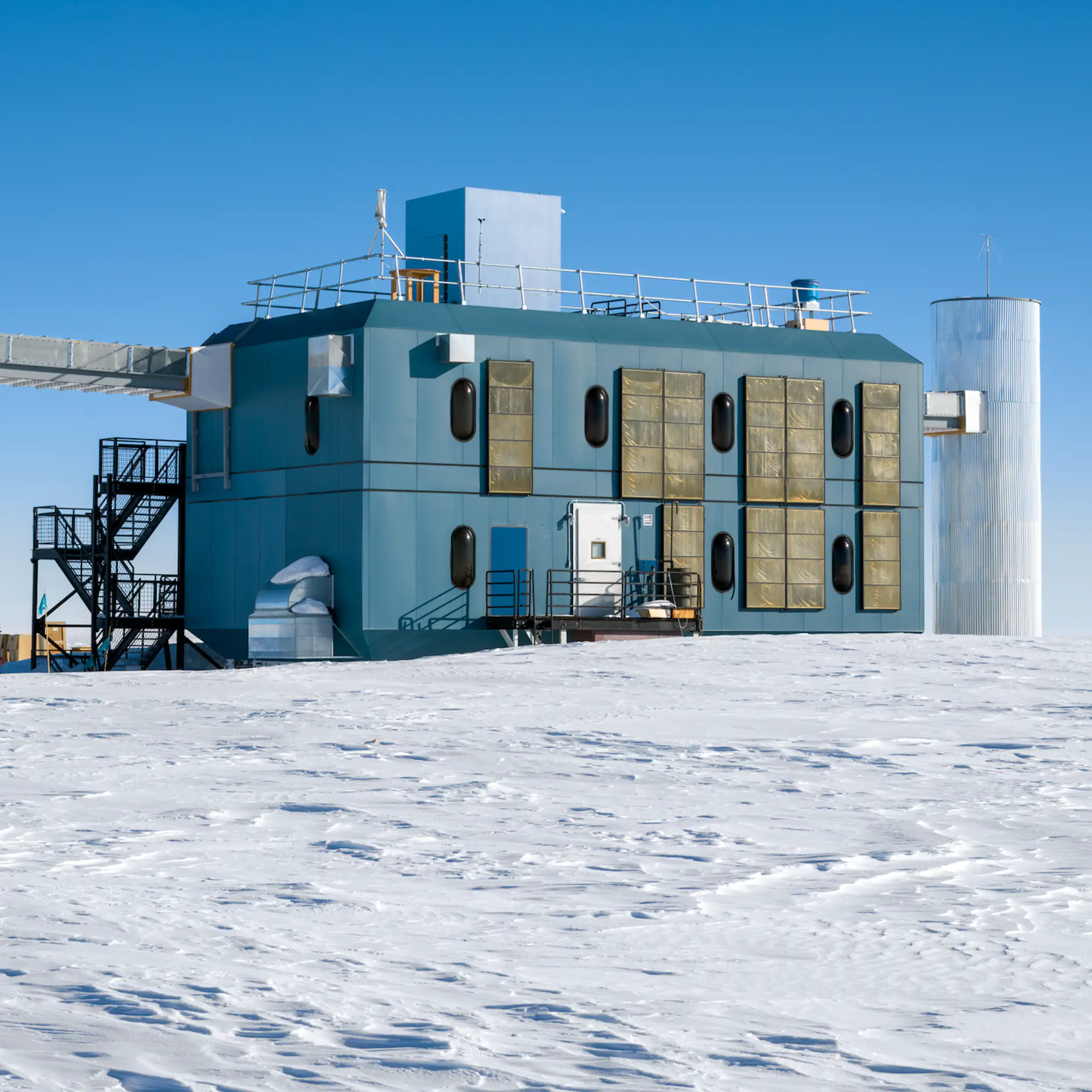 The IceCube research station, a rectangular building with three pillars attached, sitting on snowy ground.