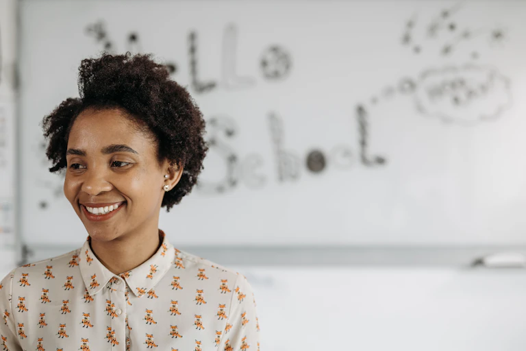 A woman stands in front of a whiteboard, smiling and looking off to the side.