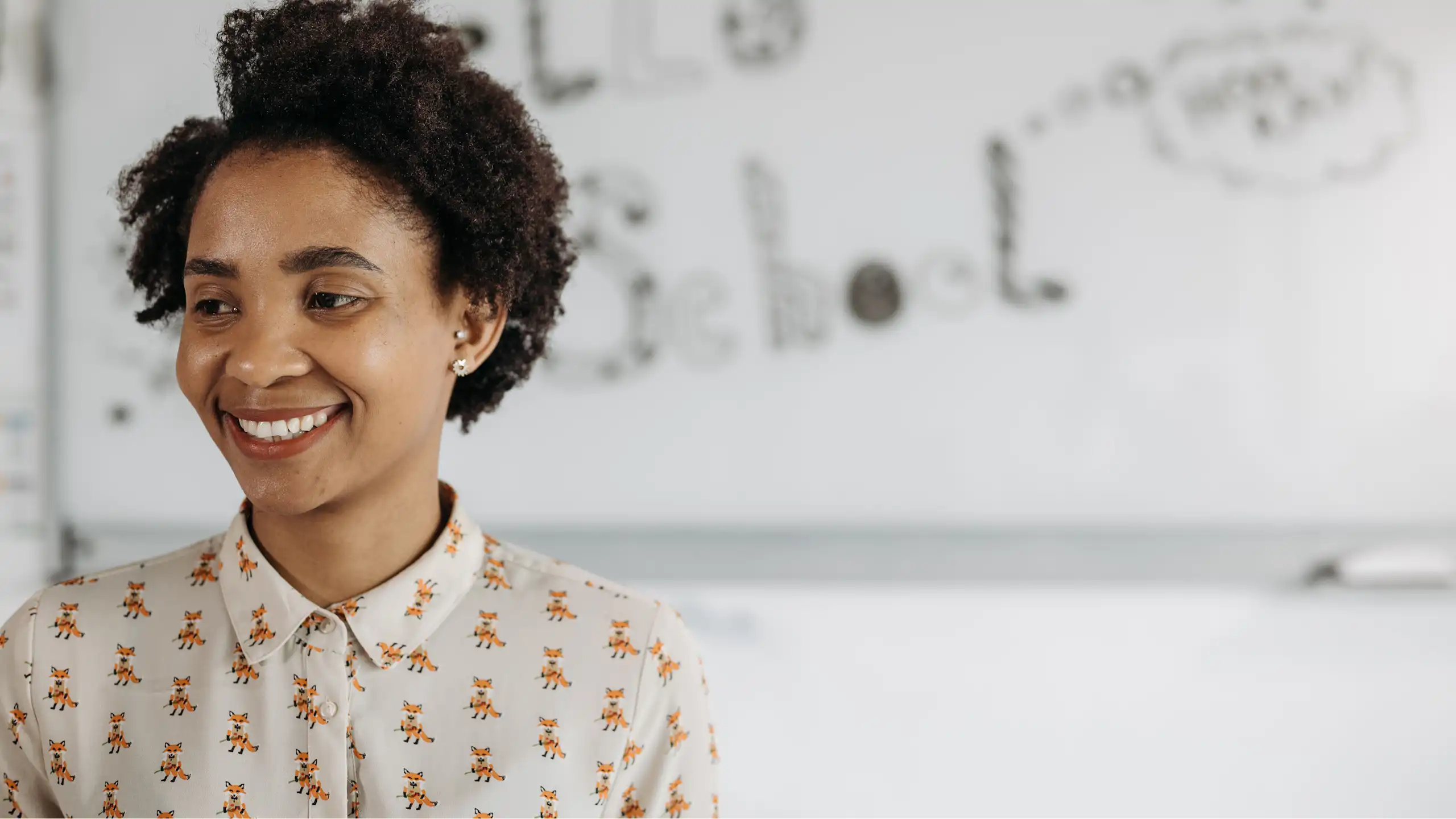 A woman stands in front of a whiteboard, smiling and looking off to the side.
