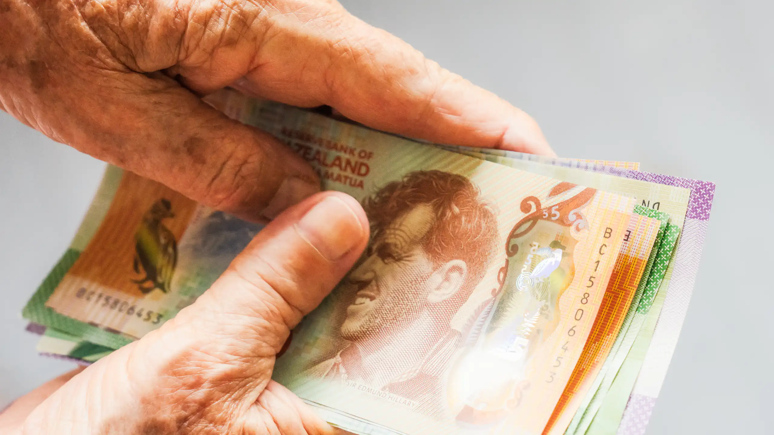 Older person's hands holding New Zealand banknotes
