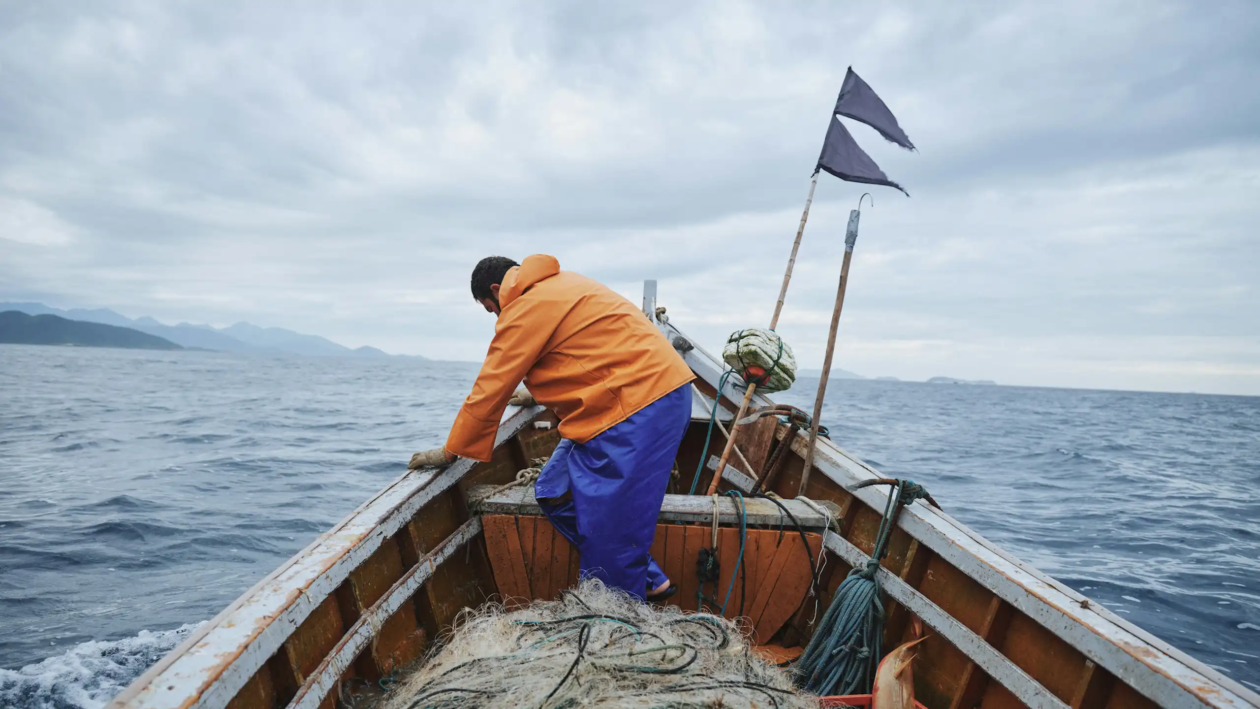 A man leans on the side of a boat filled with fishing nets, on the ocean
