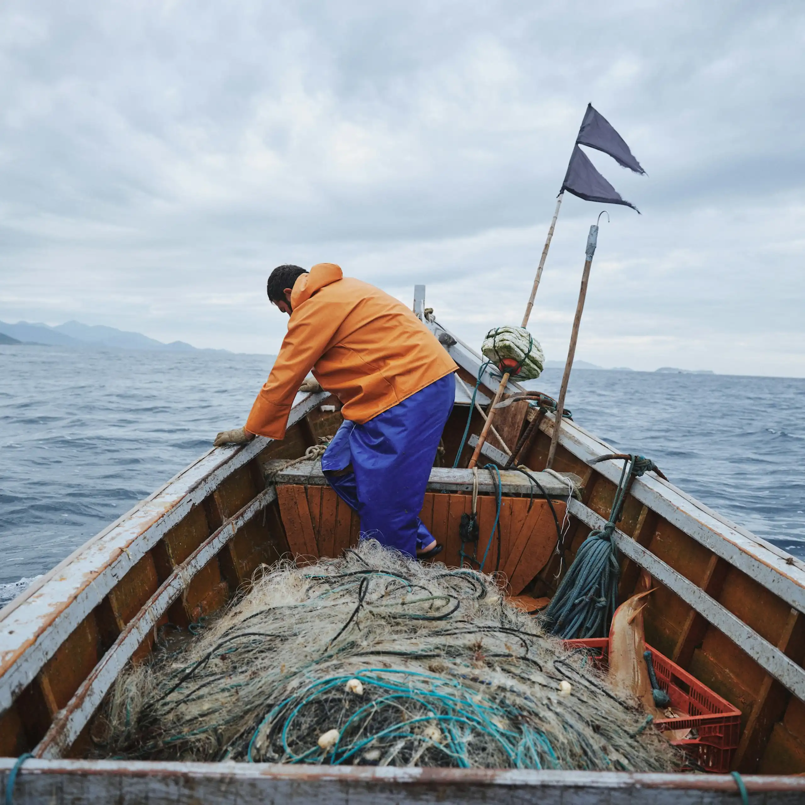 A man leans on the side of a boat filled with fishing nets, on the ocean