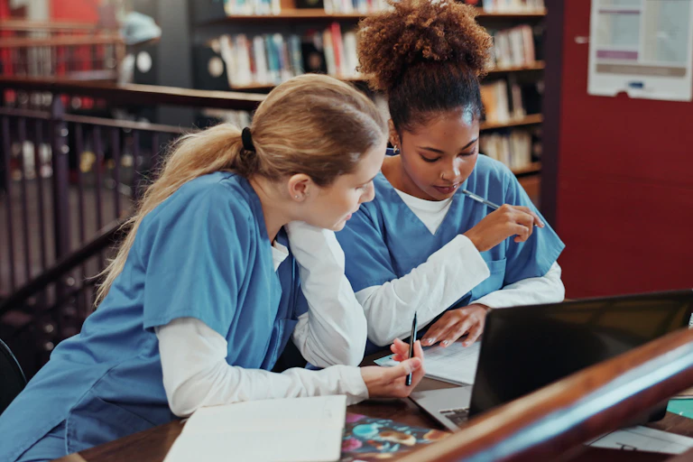 Healthcare students sit around a table discussing notes and information on a laptop.