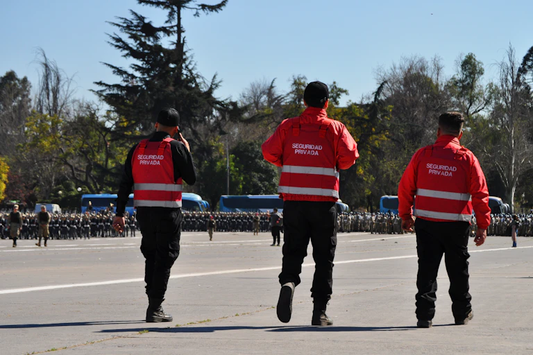 Tres guardias de seguridad privada con uniforme rojo, de espaldas.