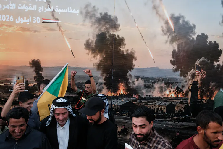 People poses for photos in front of a picture showing a war scene.