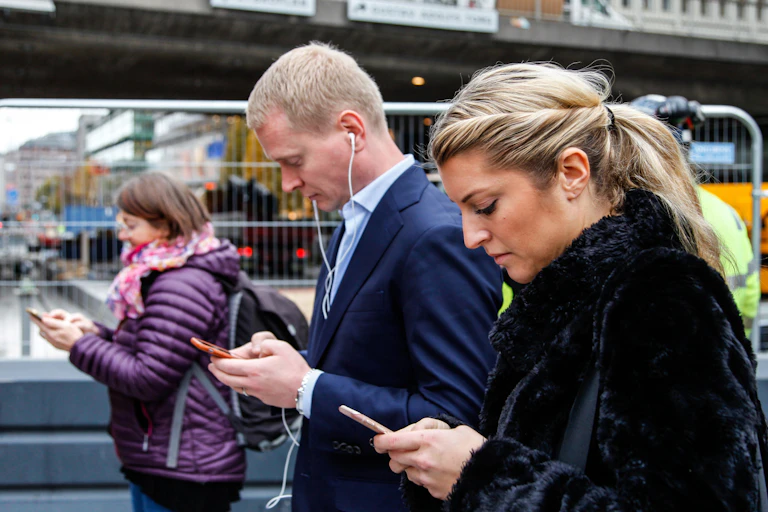 Three people glued to their phones as they walk through Stockholm city centre.