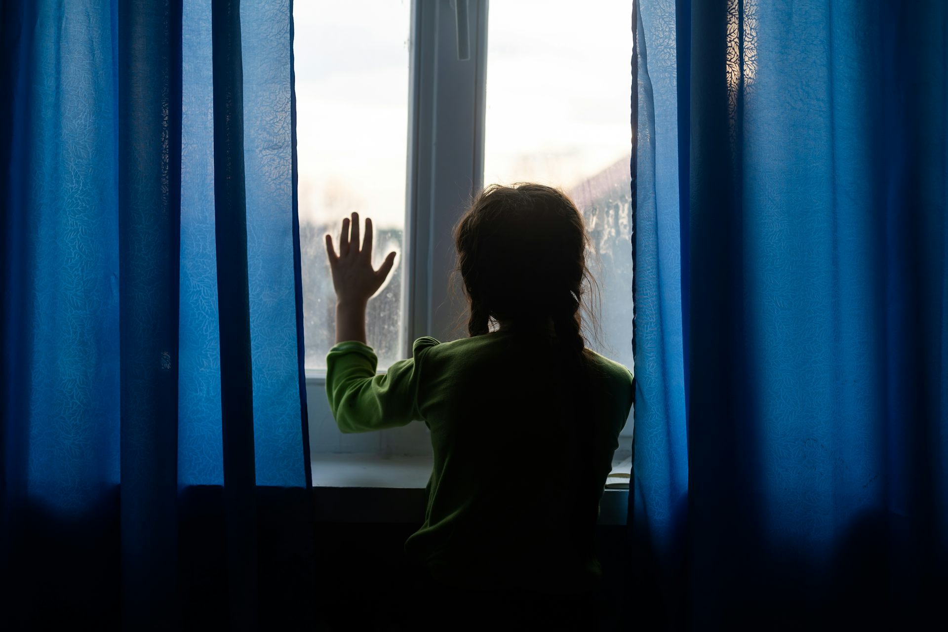 Girl seen from behind looks out of window