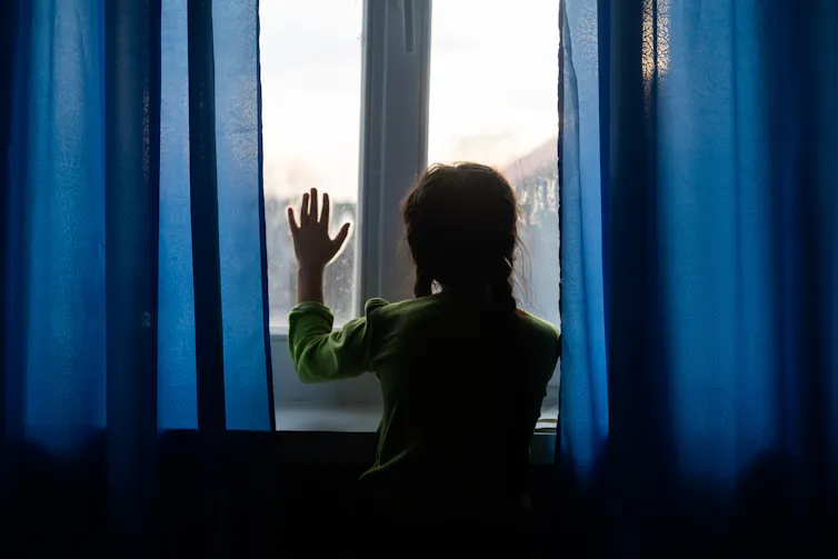 Girl seen from behind looks out of window