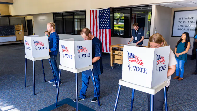 Three people stand in front of voting booths.