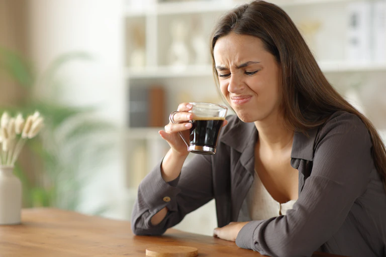 Une jeune femme fronce le nez après avoir goûté un café.