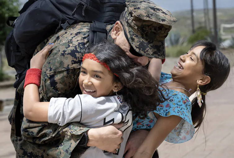 A man wearing a military uniform hugs to girls who are smiling.
