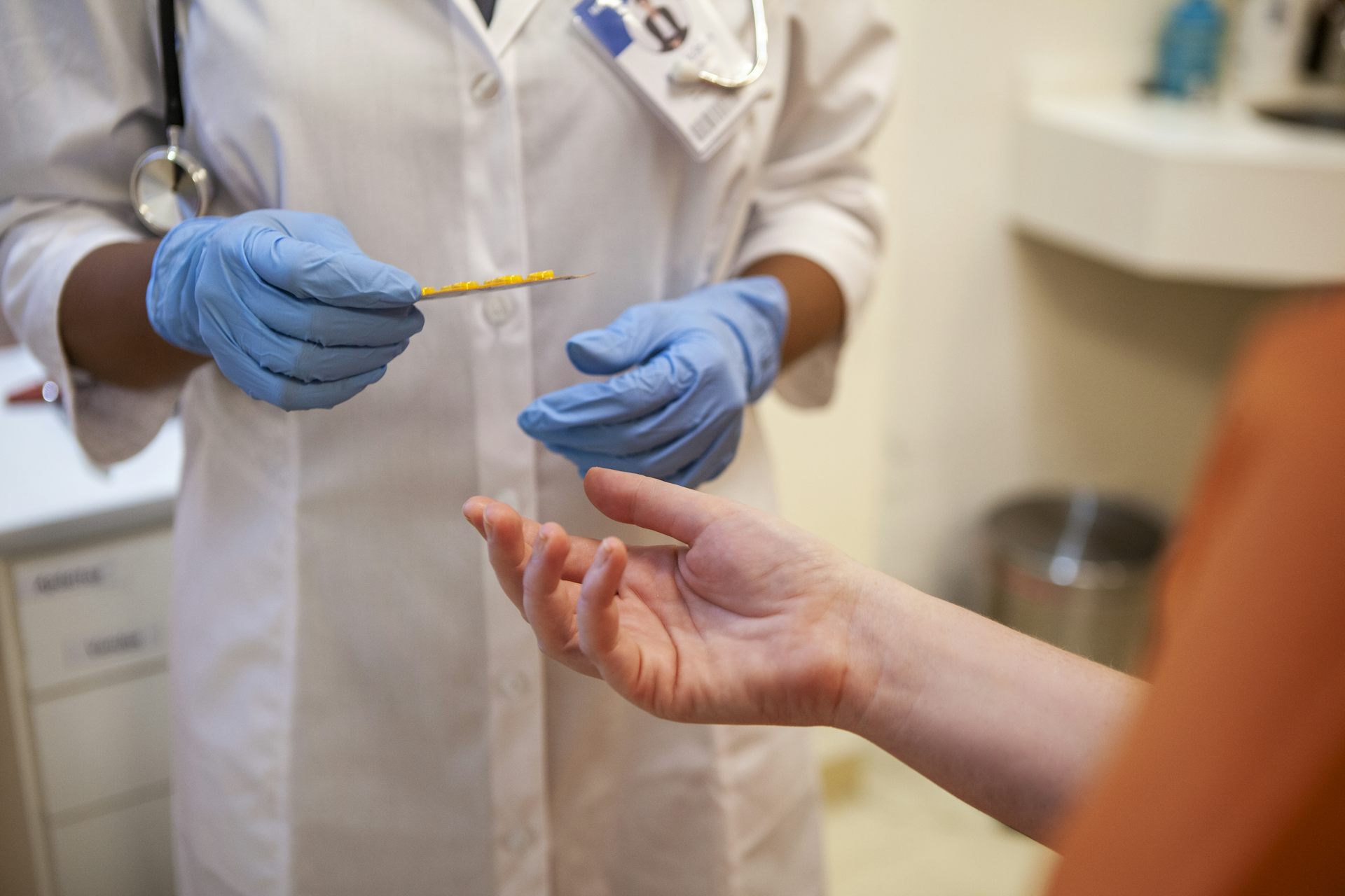 Close up shot of healthcare worker's gloved hands handing blister pack of pills to person wearing orange